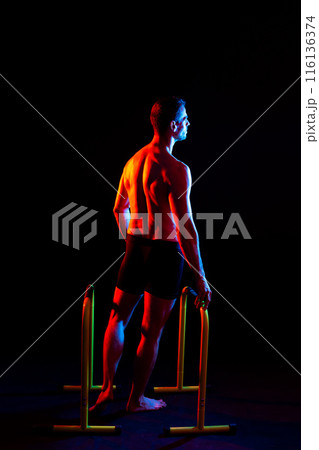 Strong male athlete shows moves on parallel bars, studio shot 116136374