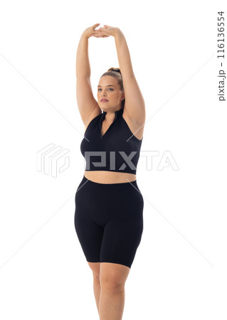 Caucasian plus-size model stretches arms up, clad in black sportswear on white background Caucasian plus-size model stretches arms up, clad in black sportswear on white background 116136554