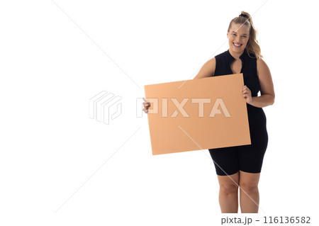 A young Caucasian plus size model holds blank sign, smiling on a white background, copy space 116136582