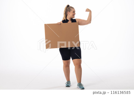 Plus size Caucasian woman shows strong arm, holds sign on white background, copy space Plus size Caucasian woman shows strong arm, holds sign on white background, copy space 116136585