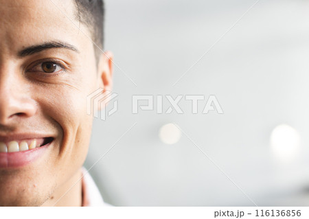 A biracial young man wearing a pink shirt, smiling at the camera in a modern business office with co 116136856