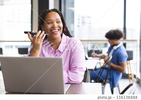 Biracial woman with braids talks on phone, works on laptop in a modern office Biracial woman with braids talks on phone, works on laptop in a modern office 116136888