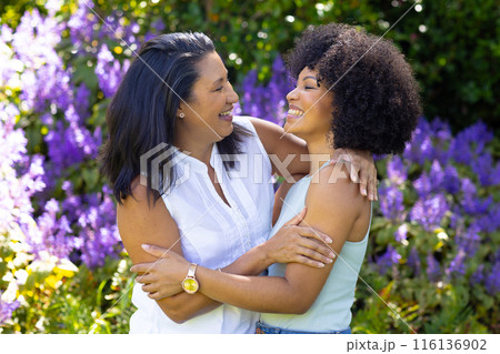 A mature biracial woman and her young daughter laugh and hug at home in garden 116136902