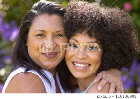 Mature biracial mother and daughter embracing, smiling in garden Mature biracial mother and daughter embracing, smiling in garden 116136909
