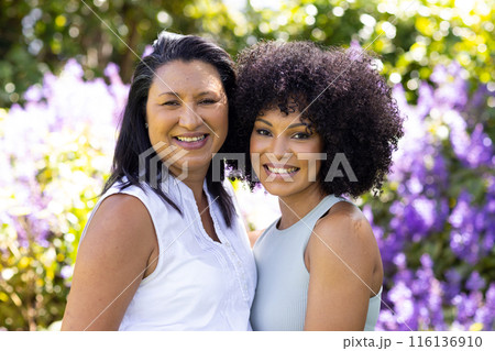 Mature biracial woman and young biracial woman stand, smiling in garden 116136910