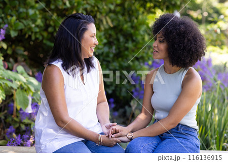 Mature and young biracial women, mother and daughter, holding hands in garden 116136915