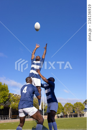 Three young African American men play rugby, one leaps for the ball 116136919