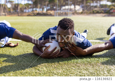 Three African American young male athletes train with rugby ball on a grass field 116136921