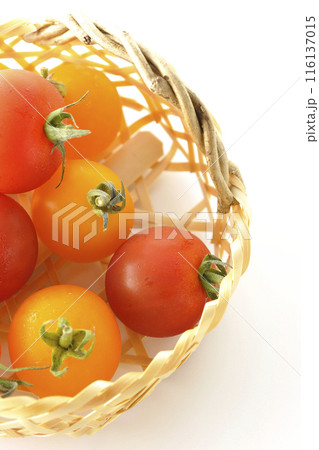 竹かごに沢山入っている黄色と赤色のミニトマトを白背景で撮影 116137015