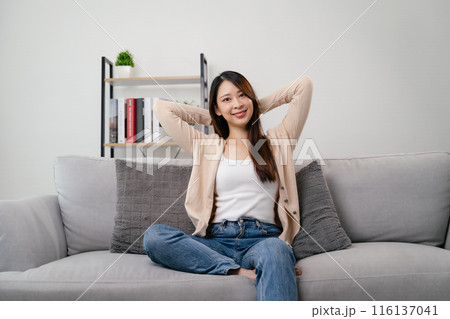 A portrait of beautiful young asian woman is sitting on a couch and smiling. 116137041