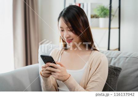 A woman is sitting on a couch and looking at her cell phone. A woman is sitting on a couch and looking at her cell phone. 116137042