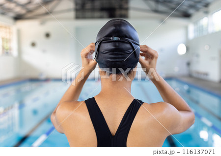 Biracial young female swimmer adjusting swim cap, standing poolside indoors Biracial young female swimmer adjusting swim cap, standing poolside indoors 116137071