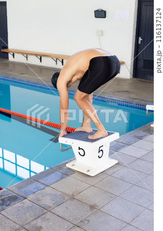 Caucasian young male swimmer preparing to dive into the pool indoors Caucasian young male swimmer preparing to dive into the pool indoors 116137124