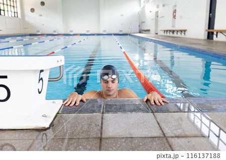 Caucasian young male swimmer wearing cap and goggles, resting at swimming pool edge 116137188