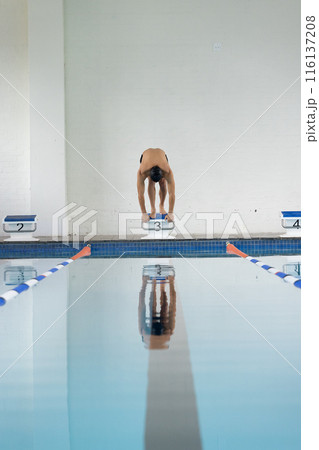 Caucasian boy in goggles readies to dive into pool from indoor starting block, copy space Caucasian boy in goggles readies to dive into pool from indoor starting block, copy space 116137208