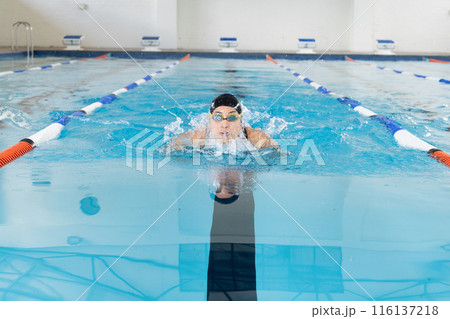 Biracial girl with goggles swims breaststroke in pool, copy space 116137218