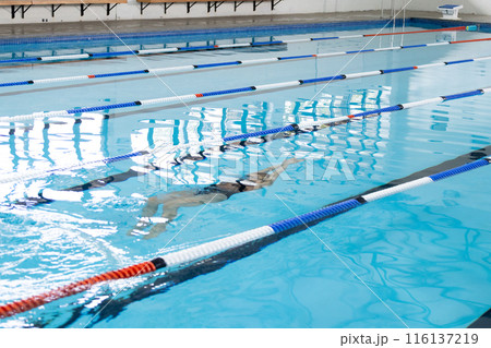 Biracial girl in swimsuit and cap trains in indoor pool, copy space 116137219