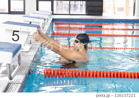Young Caucasian male swimmer at pool edge, gearing up indoors 116137221