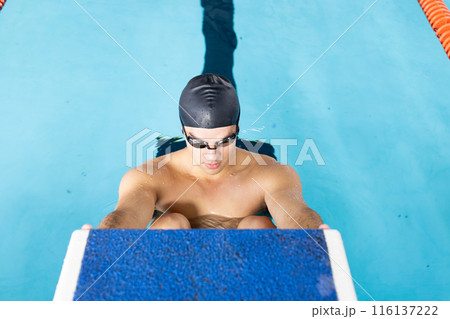 Caucasian young male swimmer preparing to dive into indoor swimming pool 116137222