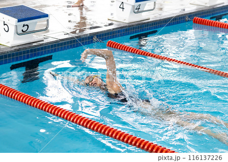 A biracial young female swimmer wearing goggles, training in indoor swimming pool 116137226