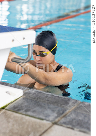 Young biracial female swimmer, grasping pool edge, ready to train Young biracial female swimmer, grasping pool edge, ready to train 116137227