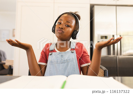An African American girl wearing headphones, shrugging during video call at home 116137322