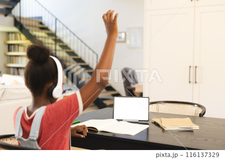 African American girl in headphones raises hand in tablet-based online lesson, copy space 116137329