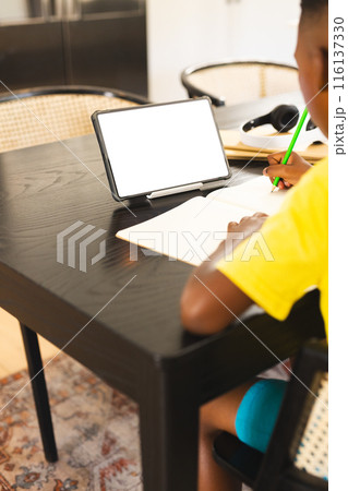 African American boy in yellow shirt writing in notebook using tablet, copy space 116137330