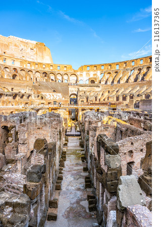 A view of the Colosseum in Rome at sunset, looking down into the arena. The ancient amphitheater is bathed in warm light, with visitors exploring the historic site. A view of the Colosseum in Rome at sunset, looking down into the arena. The ancient amphitheater is bathed in warm light, with visitors exploring the historic site. 116137365