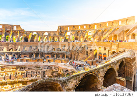 A view of the Colosseum in Rome, Italy, during a beautiful sunset. The ancient amphitheater is bathed in warm light as the sun sets on the horizon. 116137367