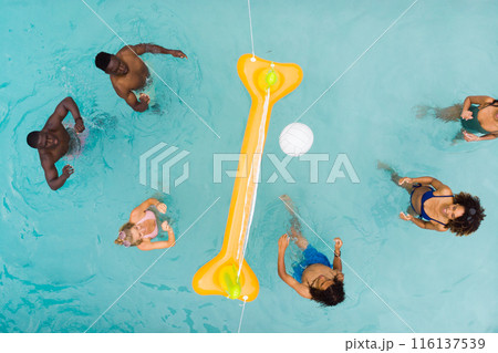 Overhead of happy diverse friends playing fun game of volleyball in sunny swimming pool, copy space Overhead of happy diverse friends playing fun game of volleyball in sunny swimming pool, copy space 116137539