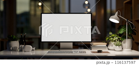 A modern office at night features a computer mockup, accessories, and a dim light from a table lamp. A modern office at night features a computer mockup, accessories, and a dim light from a table lamp. 116137597
