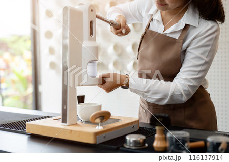 A close-up image of an Asian female barista is making a coffee cup with a machine in a coffee shop. 116137914