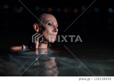 Caucasian woman in a white dress bathes in the night sea. The girl in the water in the evening poses beautifully at sunset on vacation. Relaxation, rest and enjoyment, meditation in the river. Caucasian woman in a white dress bathes in the night sea. The girl in the water in the evening poses beautifully at sunset on vacation. Relaxation, rest and enjoyment, meditation in the river. 116138439