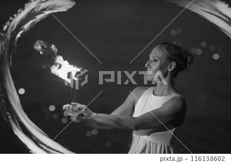 Caucasian woman in a white dress juggles with fireballs in the sea. Fire and water at night. Fire show on the waterfront. High quality FullHD footage. slow motion video 116138602