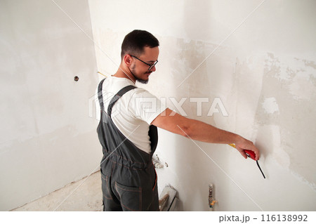 Construction worker measuring wall with tape measure, white background. Back view. Skilled builder using tape measure on white wall 116138992