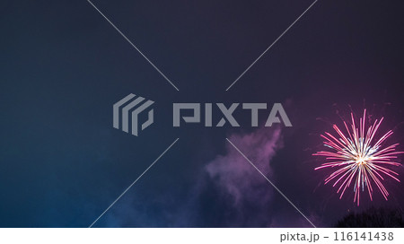A single firework that bursts into night sky. Fireworks with a white core and pink streaks create a starburst effect. A trail of smoke indicates path of firework, adding to the spectacular moment. 116141438