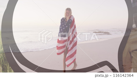 Caucasian female wrapped in American flag stands on beach, smiling Caucasian female wrapped in American flag stands on beach, smiling 116142364