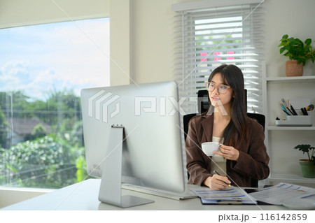 Portrait of Asian female entrepreneur drinking coffee and working at her office Portrait of Asian female entrepreneur drinking coffee and working at her office 116142859