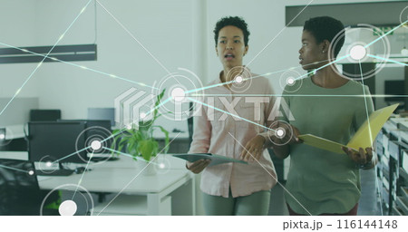 Image of connected dots over diverse female coworkers discussing reports while walking in office 116144148