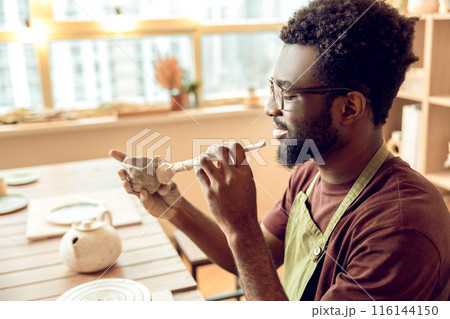 Male sculptor working on a new clay mug in his office Male sculptor working on a new clay mug in his office 116144150