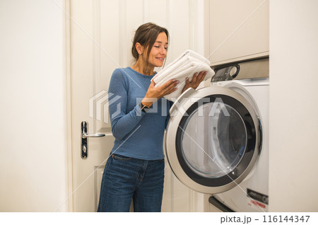 Woman smelling newly washed towels and looking contented 116144347