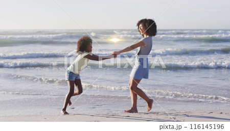Image of light trails over african american woman and her daughter at beach 116145196