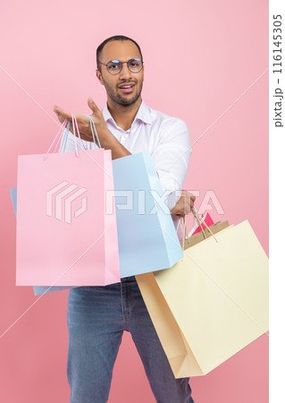Uncertain African American man wearing shirt and glasses holding shopping bags standing with questioning expression questioning expression Uncertain African American man wearing shirt and glasses holding shopping bags standing with questioning expression questioning expression 116145305