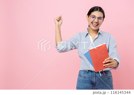 Extremely happy girl in casual shirt holding books rejoicing success clenched fist copy space Extremely happy girl in casual shirt holding books rejoicing success clenched fist copy space 116145344