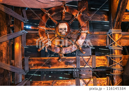 wooden steering wheel with skull in interior of captain's cabin on ancient medieval pirate ship wooden steering wheel with skull in interior of captain's cabin on ancient medieval pirate ship 116145384