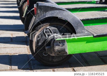 wheels of green electric scooters standing in row for rental the sidewalk in city in summer close-up 116145523
