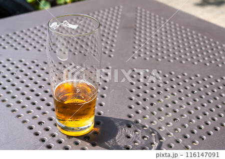 Beer glass in sunny day, cold pint glass with remaining beer on outdoor table, cool condensation 116147091