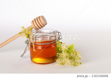 A jar of liquid honey from Linden flowers, stick with honey and fresh flowers on a white background.Copy space.Close up A jar of liquid honey from Linden flowers, stick with honey and fresh flowers on a white background.Copy space.Close up 116148006