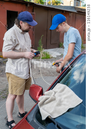 Dad and teenage son work together on the street near the garage. Outdoor activity. Family spend time. Helping and teach. Repairing a hose and pump for hand washing a car from a plastic bottle 116149238